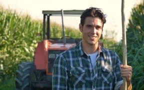 Jeune homme devant un tracteur dans un champ